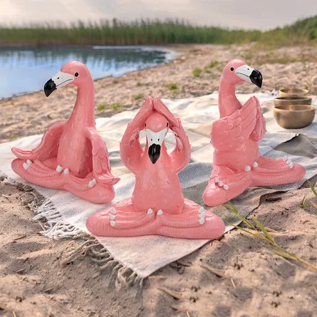 Three pink flamingos are sitting in the sand.
