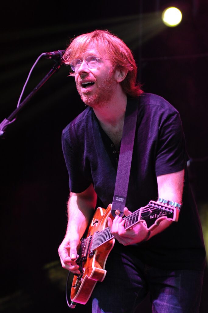 A man with red hair and glasses playing guitar.